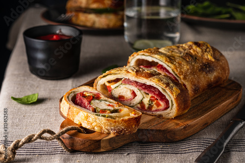 Traditional Italian Stromboli stuffed with cheese, salami, red pepper and spinach. Photo in a dark style.