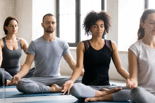 Diverse young people meditating, sitting in Lotus pose, practicing yoga