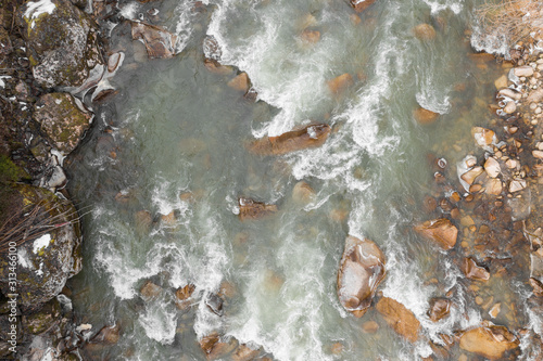Top-down drone view of rapids of mountain river with wet boulders and pebble shore. Beautiful and powerful azure river stream with large stones. Nature concept