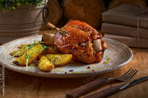 Pork knuckle with baked potatoes on rustic kitchen table at dark wooden background, front view. Pork leg done, German food