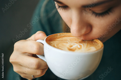 Close up girl is drinking coffee. She enjoys her morning cappuccino or flat white.