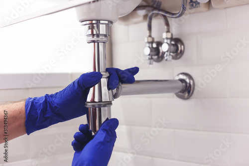 Plumber repairs and maintains chrome siphon under the washbasin. Plumber at work in bathroom, plumbing assemble and install concept