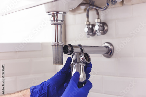 Plumber repairs and maintains chrome siphon under the washbasin. Plumber at work in bathroom, plumbing assemble and install concept