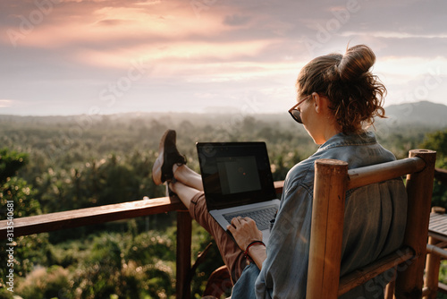 Young business woman working at the computer in cafe on the rock. Young girl downshifter working at a laptop at sunset or sunrise on the top of the mountain to the sea, working day.