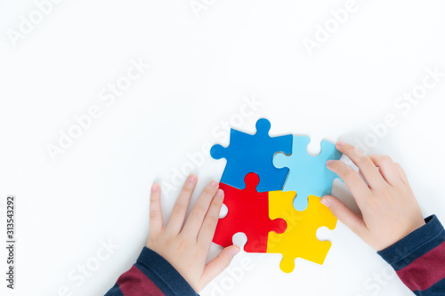 Top view, hands of an autistic child play colorful puzzle which is a symbol of public awareness for autism spectrum disorder - World Autism Awareness day on April 2, Understanding and Acceptance.