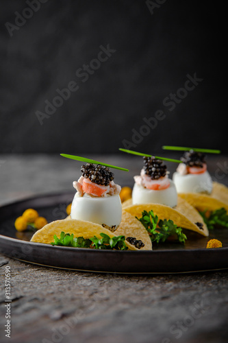 Luxurious appetizer of quail eggs with a paste of squid, shrimp and black caviar on potato and cheese chips.