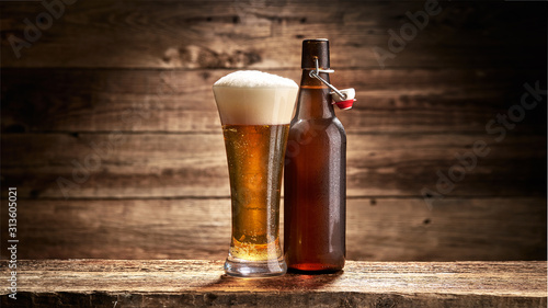Szklanka pełna piwa i butelka na tle starych desek