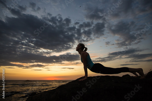 Yoga woman doing fitness exercise on the ocean coast at dusk..