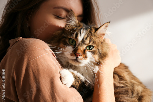 Portrait of young woman holding cute siberian cat with green eyes. Female hugging her cute long hair kitty. Background, copy space, close up. Adorable domestic pet concept.