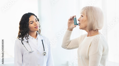 Physician examining mature woman using blue asthma inhaler