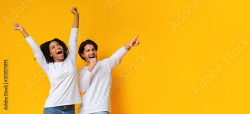Multiracial couple dancing and singing together, having fun over yellow background