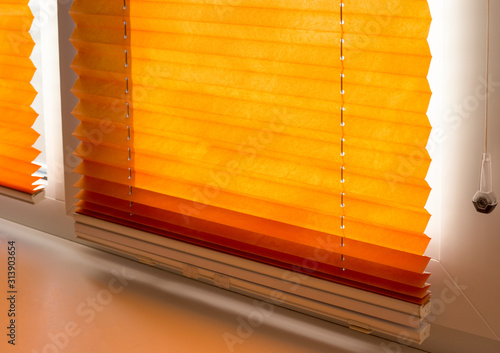 Pleated blinds with orange folded fabric on the window close up. Cordless bottom up top down pleated shade with white lower bar.