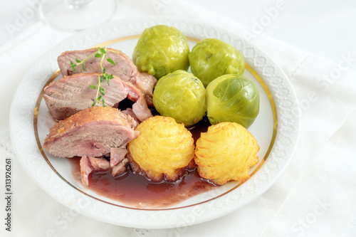 Tenderly roasted duck breast fillet with brussels sprout and duchess potatoes on a white plate, a festive dinner for holidays