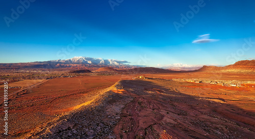 Red dirt and red rocks catch the light of a setting sun as rare snow caps distant rock and mountains in Southern Utah not far from St. George.