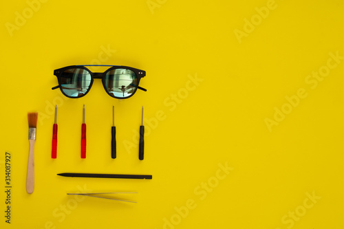 Top view sunglasses over yellow background repair tools. Technical service concept or optometry store service.