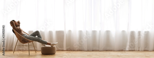 Young Asian Girl Relaxing In Modern Wicker Chair Near Window