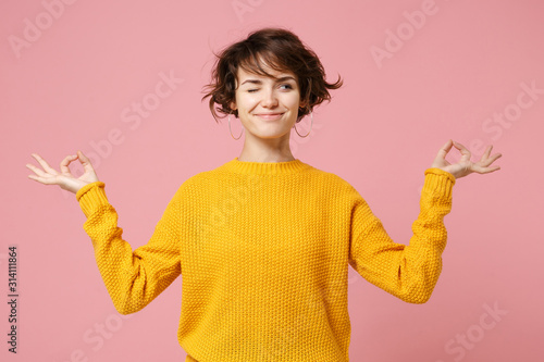 Funny young brunette woman girl in yellow sweater posing isolated on pastel pink background. People lifestyle concept. Mock up copy space. Hold hands in yoga gesture relaxing meditating looking aside.