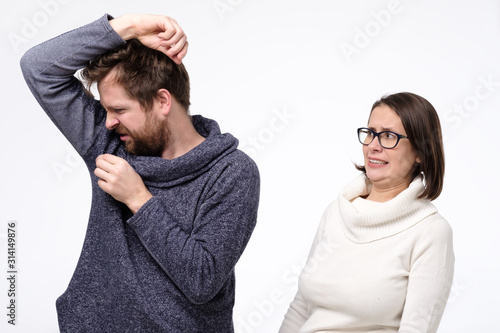 Young man with sweat stain on his clothes and caucasian woman feeling bad smell.