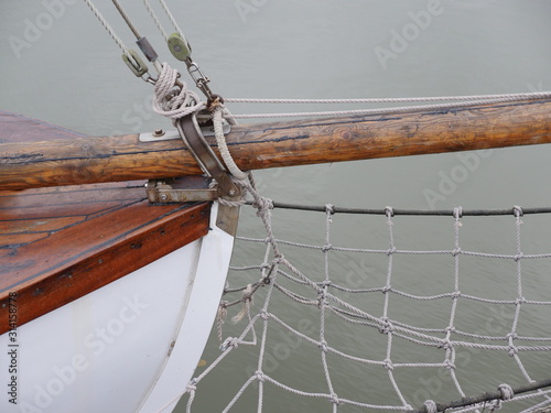 Partial view of the bow of a historic sailing ship, metal bow fitting to hold the bowsprit, stage, bow net. Also visible deck planks, white hull.