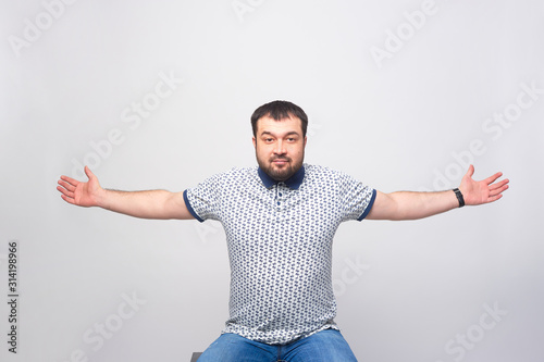 A man warmly greets the viewer with his arms spread wide over a white background.