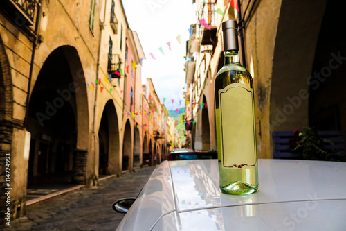 Primo piano di una bottiglia di vino bianco appoggiata sul tetto di una macchina nel viale dei portici di pieve di teco, viaggi e architettura sui monti della Liguria in Italia