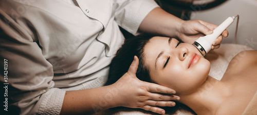 Side view portrait of a charming woman doing a electroporation procedure on her face while cleaning with closed eyes on a spa bed in welens spa center.