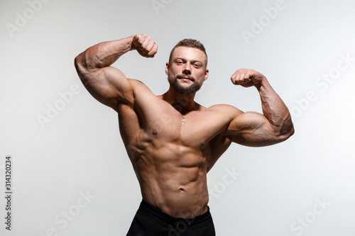 Young muscular bodybuilder guy demonstrates his muscles isolated on a light gray background.