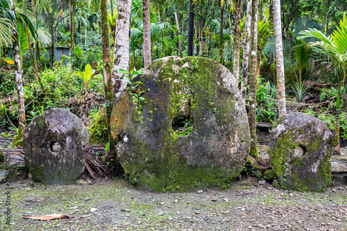 Three giant prehistoric megalithic stone coins or money Rai, under trees overgrown in jungle. Yap island, Federated States of Micronesia, Oceania, South Pacific Ocean