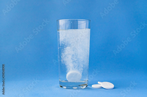 Fizzy aspirin in a glass of water on a blue background. Vertical format and soft focus.