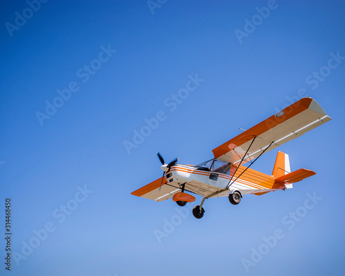 light single private orange plane in clear blue sky