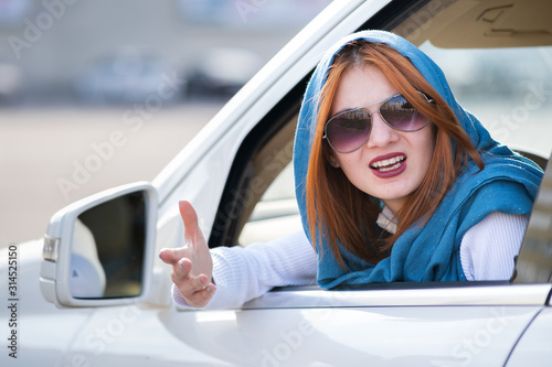 Closeup portrait of pissed off displeased angry aggressive woman driving a car shouting at someone with hand fist up. Negative human expression consept.