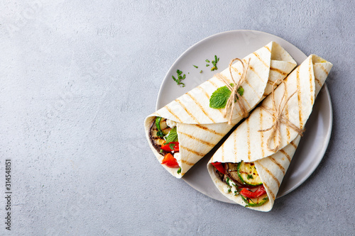 Wrap sandwich with grilled vegetables and feta cheese on a plate. Grey background. Copy space. Top view.