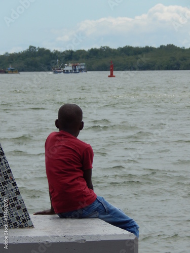 Nino sentado contemplando el paisaje del océano Pacifico en Buenaventura Colombia.