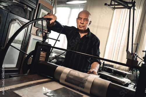 Man working on lithography machine looking camera serious balck and white photo