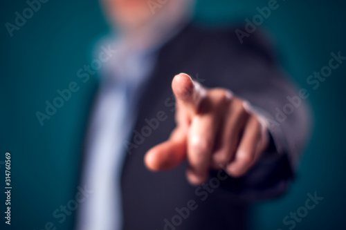 Businessman in suit point finger at camera in front of black background