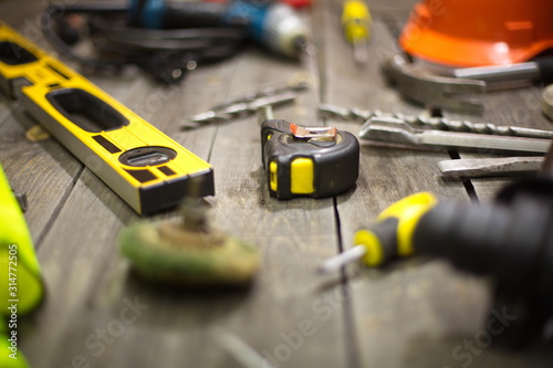 Tools on the table. On the table is: a building level, a tape-measure, a drills on concrete. In no focus: screwdriver, helmet, grinding disc, hammer drill.