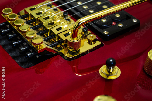 Red electric guitar with a golden tremolo. Golden Floyd Rose.