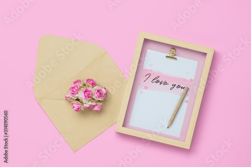 Mockup photo frame with kraft rose flower in brown envelope for Valentines day concept. Top view of mock up photo frame with craft decoration and on pastel pink background. Flat lay with copy space.