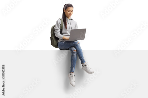 Female student sitting on a blank board and using a laptop computer