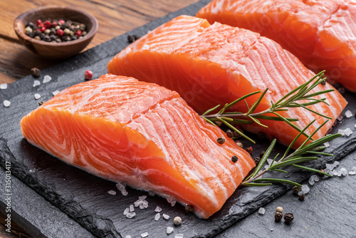 Fresh salmon fillets on black cutting board with herbs and spices.