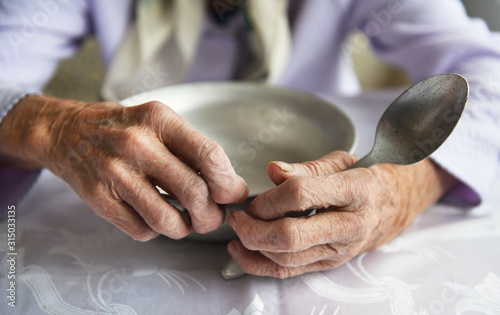 View from above.The hands of an old grandmother of 90 years are holding an empty aluminum bowl and spoon, poverty and poverty, the hunger of the older generation.