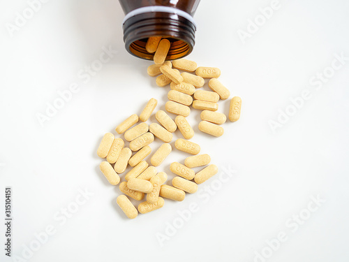 Yellow tablets vitamin C medicine from bottle on white background. Vitamin C 500 milligram pills.