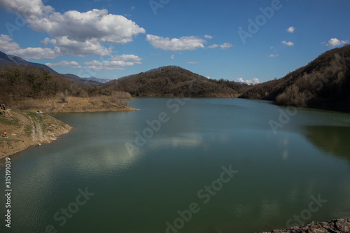Panorama of a natural dam made in a valley with visible lake behind in Vogrsko, Slovenia. some hills are seen in the background on a clear day.
