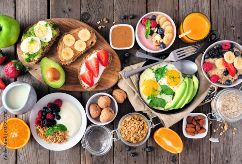 Healthy breakfast table scene with fruit, yogurts, oatmeal, smoothie, nutritious toasts and egg skillet. Top view over a wood background.
