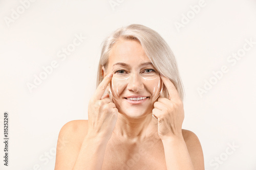 Mature woman giving herself face massage on light background