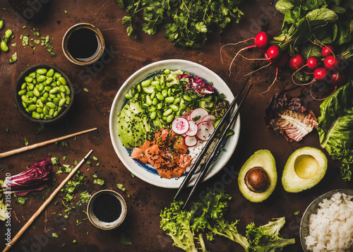 Healthy lunch, dinner. Flat-lay of salmon poke bowl or sushi bowl with vegetables, greens, sushi rice, soy sauce over rusty table background, top view. Traditional Hawaiian cuisine, clean eating food