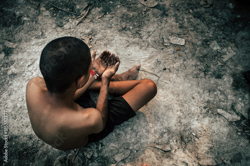 poor child or beggar begging you for help sitting at dirty slum. concept for poverty or hunger people,human rights,donate and charity for underprivileged children in third world 