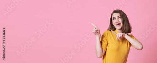 Beautiful healthy young woman smiling with his finger pointing and looking at on light pink banner background with copy space.