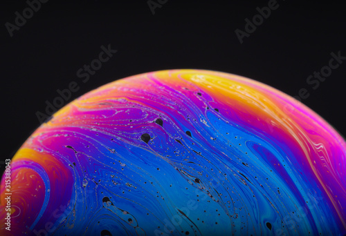 Close up macro photograph of the psychedelic rainbow of colors mixing and swirling in a soap bubble to look like a fantasy galaxy or planet isolated against a black background