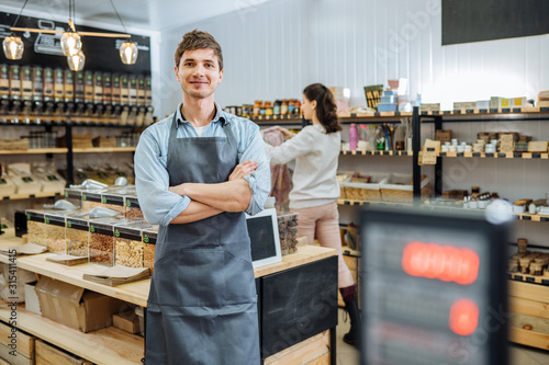 Portrait of young man owner over interior of Zero Waste Shop in Grocery Store. No plastic Conscious Minimalism